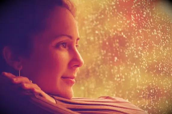 Woman looking out of rainy window with a slight smile on her face.