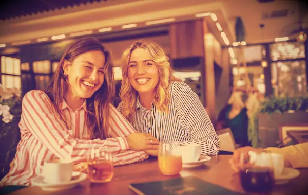 Two women laughing while sitting at a table in a coffee shop.