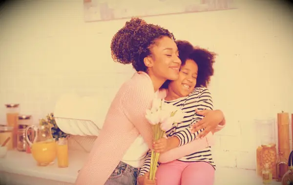 A mother hugging her daughter who is holding flowers.