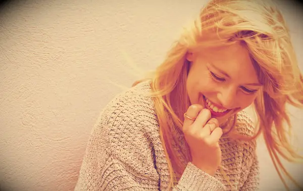 A smiling woman looking happy while standing against a white wall.
