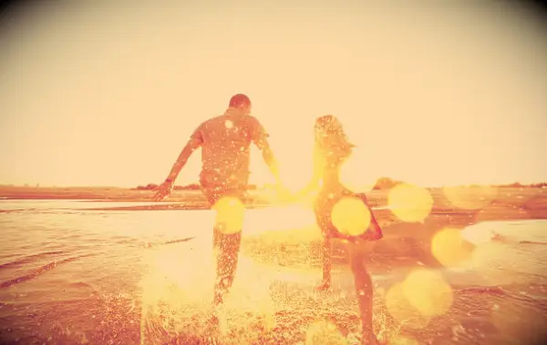 A happy couple running down the edge of the water on a beach during the golden hour.