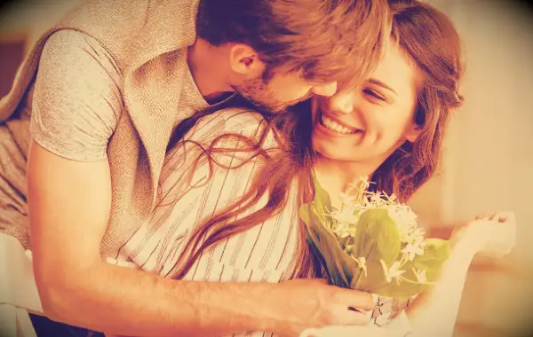 A happy man and woman hugging as the man gives the woman a bouquet of flowers.