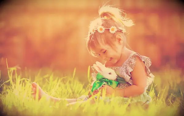 A happy little girl sitting the spring grass with a small white bunny.