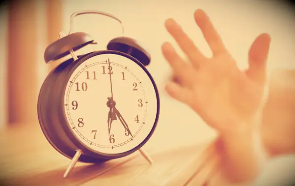A hand reaching for the alarm clock beside the bed at 6.25 in the morning.