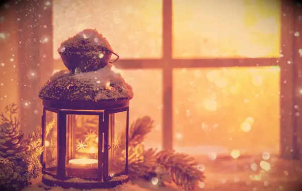 A Christmas lantern out in the snowy weather in front of a window.