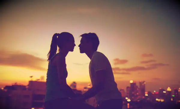 A couple about to kiss at sunset with a city in the background.