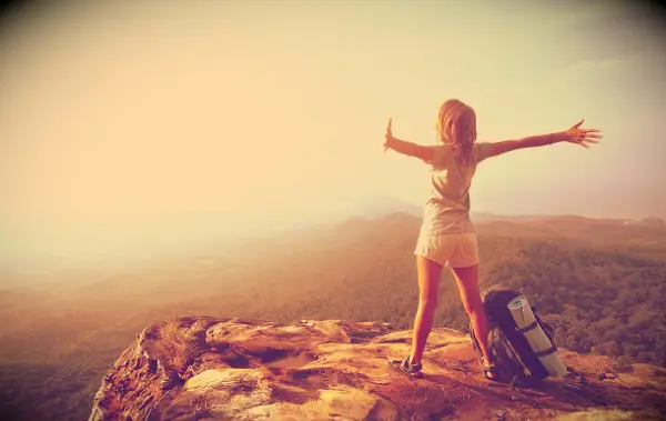 A happy woman with her arms stretched out at the top of a mountain.