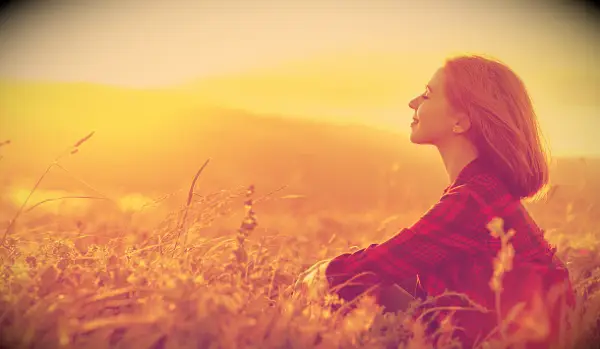 A woman sitting in a field enjoying the sunshine.