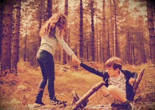 An image of a girl helping a boy up after he has fallen.