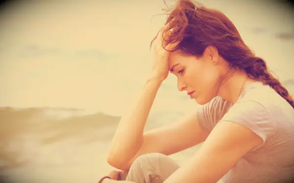 A thoughtful and upset woman sitting by the beach.