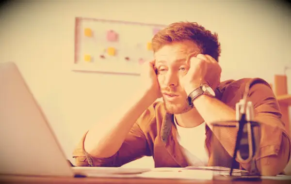 A man sitting in front of his laptop looking tired and unmotivated.